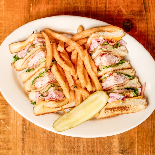 Quartered club sandwich with french fries and a pickle spear on a white plate.
