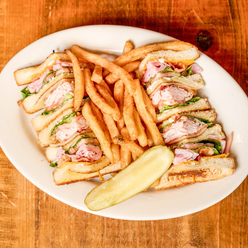Quartered club sandwich with french fries and a pickle spear on a white plate.