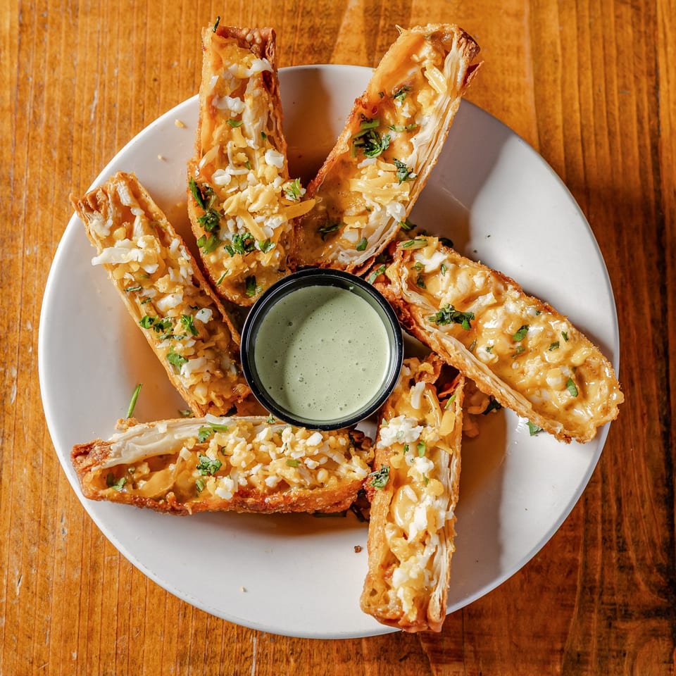 Crispy mac and cheese flautas with herbs and shredded cheese, served with green dipping sauce.