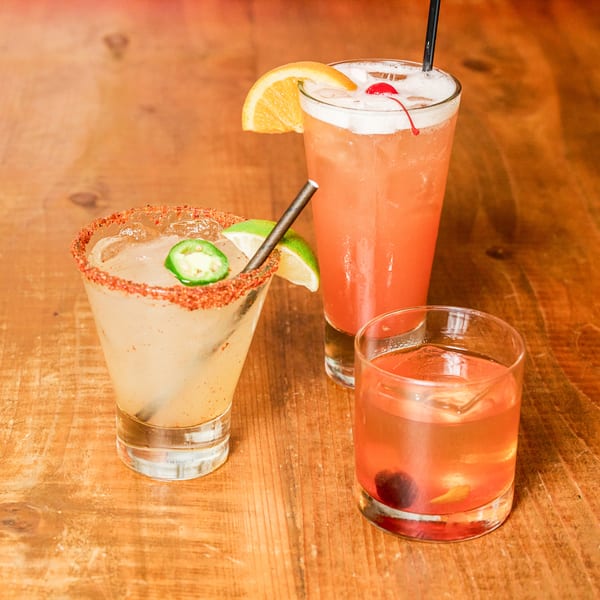 Three colorful cocktails, including a spicy margarita, on a rustic wooden table.