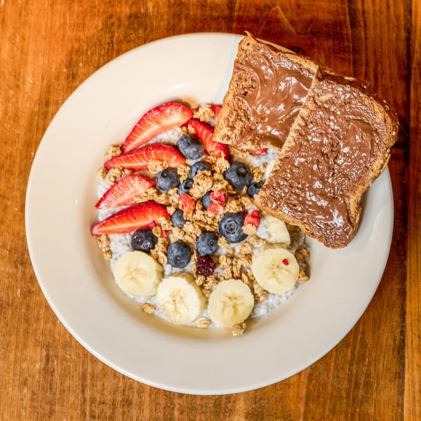 Breakfast bowl with chia pudding, granola, berries, bananas, and chocolate toast on a wooden table.