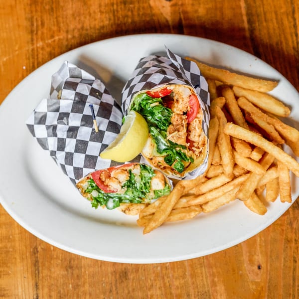 Two chicken wraps, one cut, with fries and a lemon wedge on a white plate.
