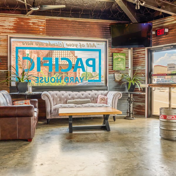 Restaurant lounge with brown armchair, grey sofa, coffee table, and corrugated metal walls.