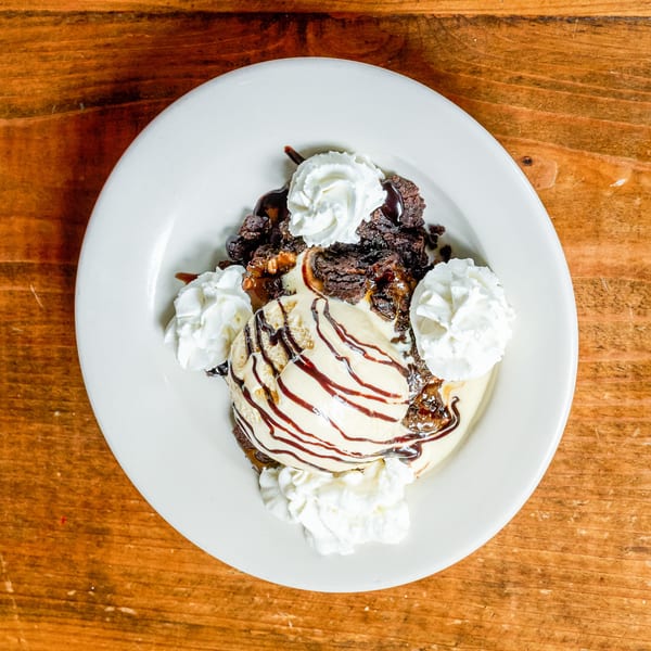 Decadent brownie dessert with vanilla ice cream, chocolate drizzle, and whipped cream on a wooden table.