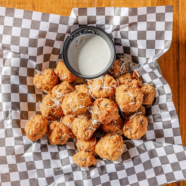 Fried mushrooms with shredded cheese and dipping sauce in a checkered paper-lined basket.